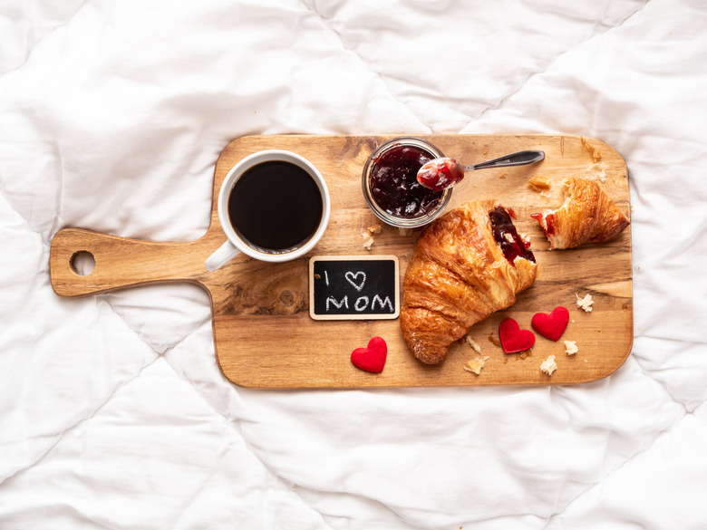 Breakfast tray with a croissant, strawberry jam and a cup of coffee on a white bedspread