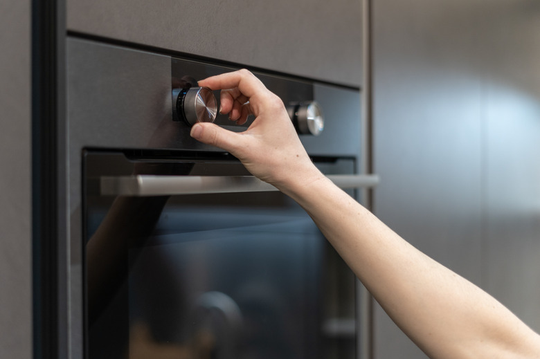 Side view photo of woman hand tuning program on control panel for built-in oven in black kitchen cabinet