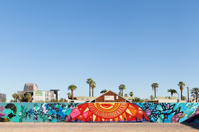 A colorful red, blue, and yellow mural with surrounding buildings and palm trees