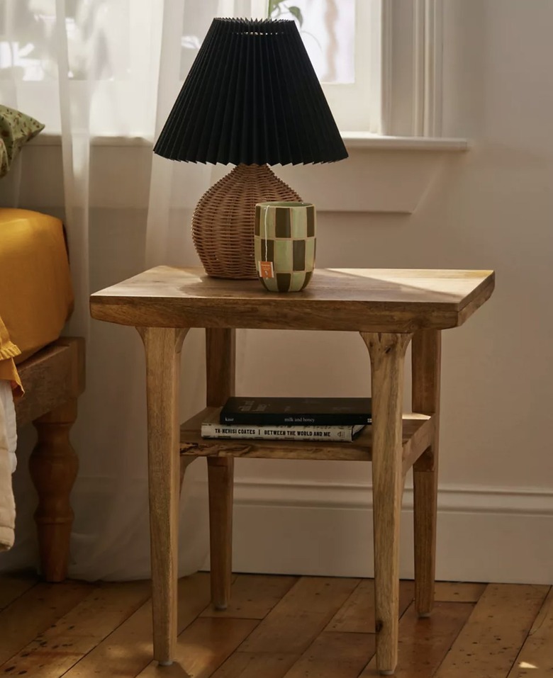 Image of a wood nightstand accessorized with a lamp, books and a coffee mug.