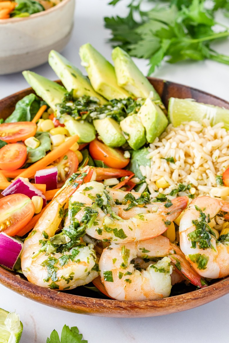 A closer look at the chimichurri shrimp in the wood bowl. The shrimp are a beautiful pink color and the sauce showcases bright green herbs.