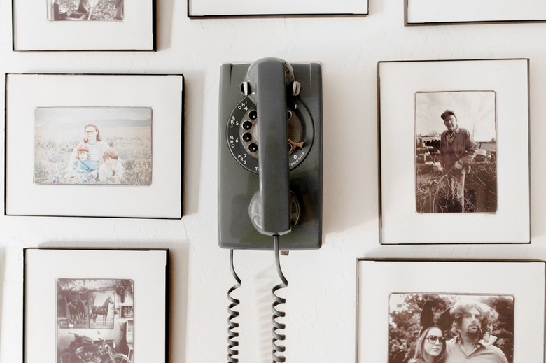 A wall of framed family photographs and a vintage gray landline phone.