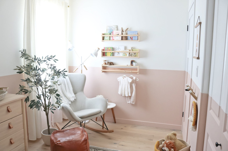 Pink and white baby nursery idea with color blocking and potted tree next to rocking chair