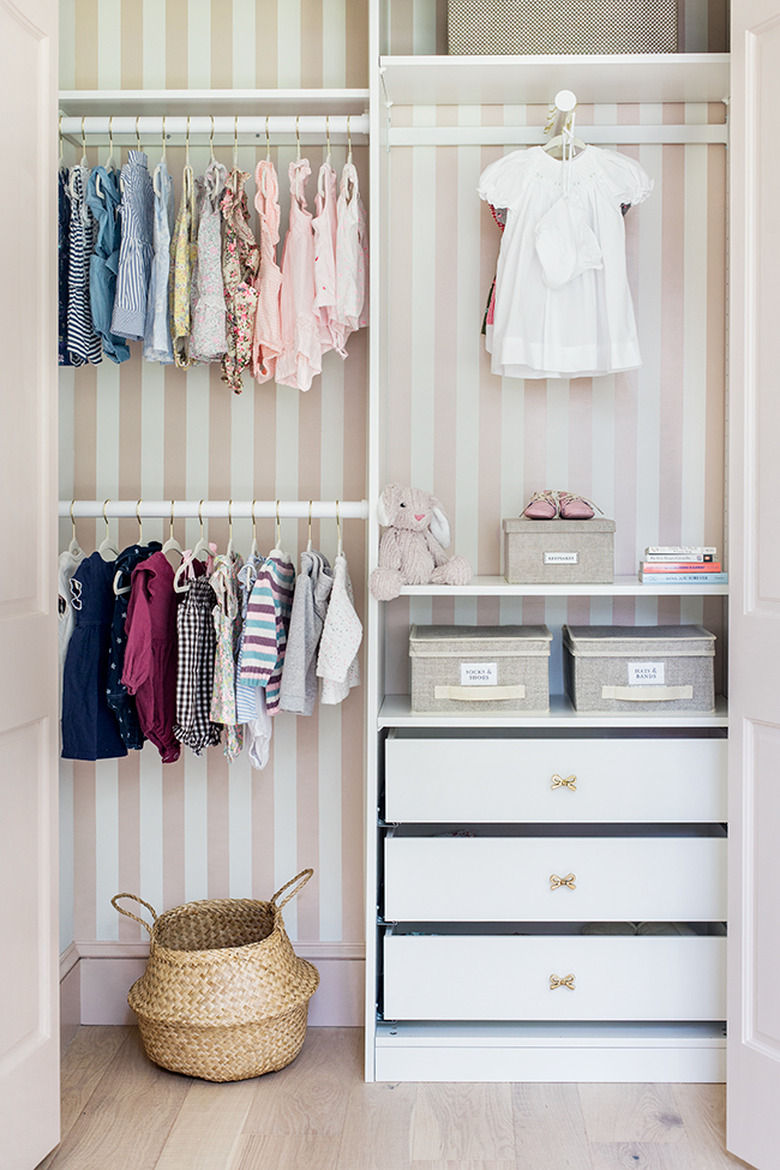 Pink and white closet nursery organization with wallpaper on back wall and drawers