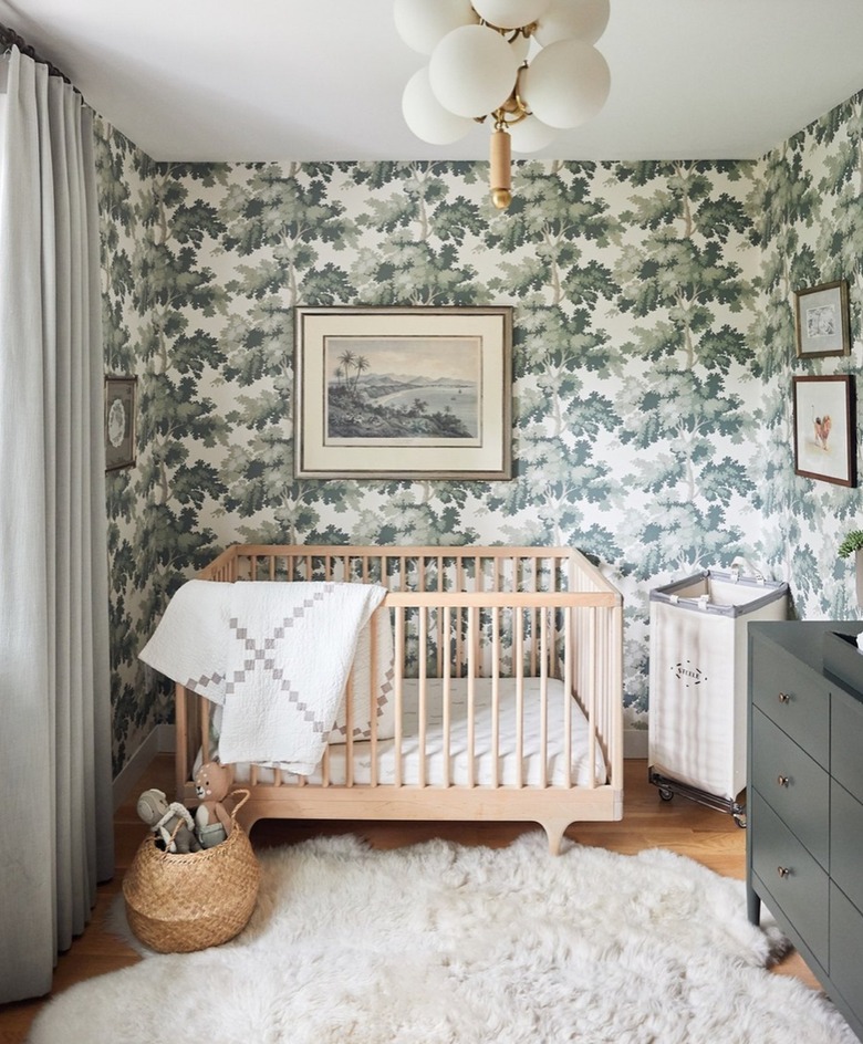 Nursery with leaf pattern wallpaper, light wood crib, sheepskin rug, green dresser.