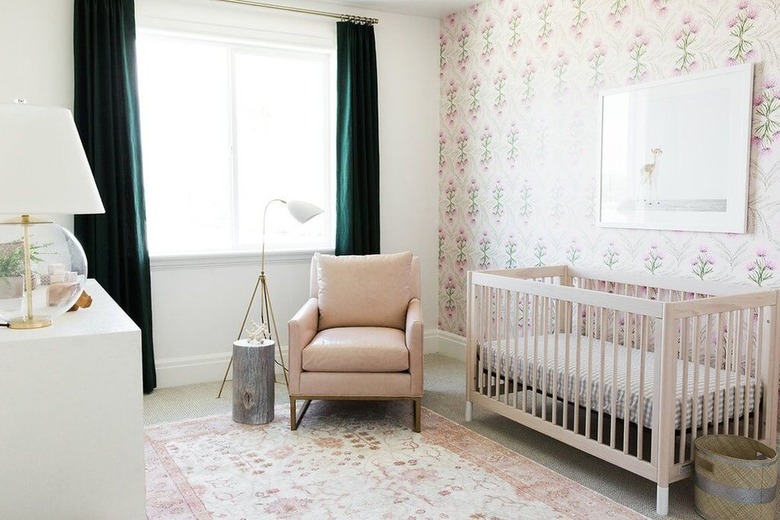 Nursery with floral wallpaper, dark green curtains, rose colored chair, floral rug.