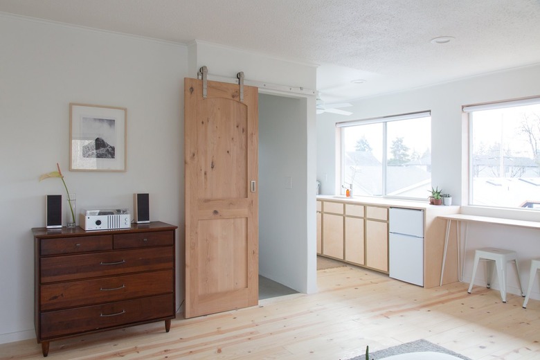 Wooden dresser with radio and speaker setup with hanging picture barn door and kitchen cabinets under large windows