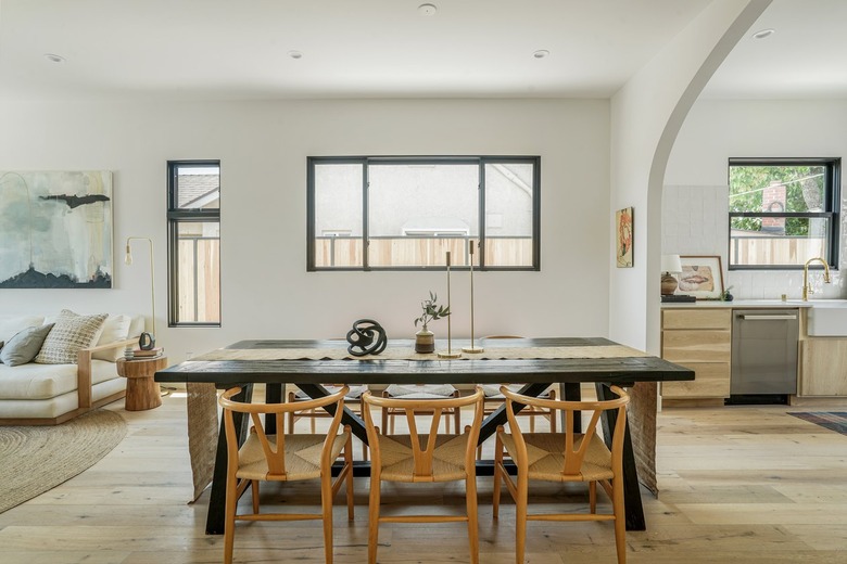 Black dining room table with honey-wood chairs, windows of varying sizes