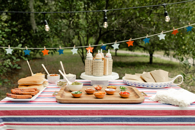 Gourmet hot dog bar with red, white and blue tablecloth, star garland, and small bowls of toppings