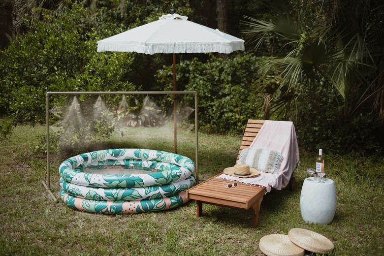 Green PVC pipe water mister over an inflatable pool next to lounge chair and fringe patio umbrella