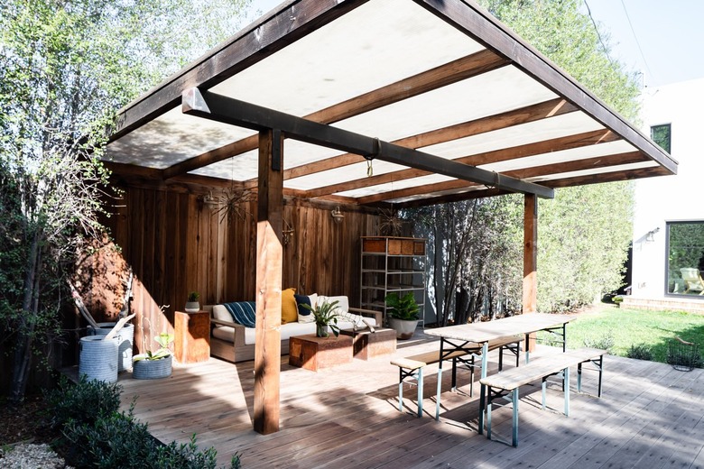 A wood pergola with wood flooring, dining bench and sofa seating