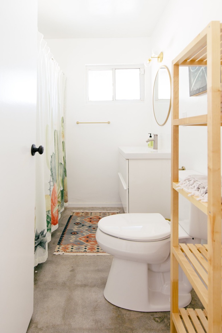 a long narrow bathroom with a concrete floor and a tall wooden shelving unit