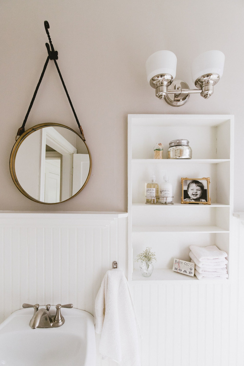 bathroom towel storage idea in white bathroom with round mirror and built-in shelving