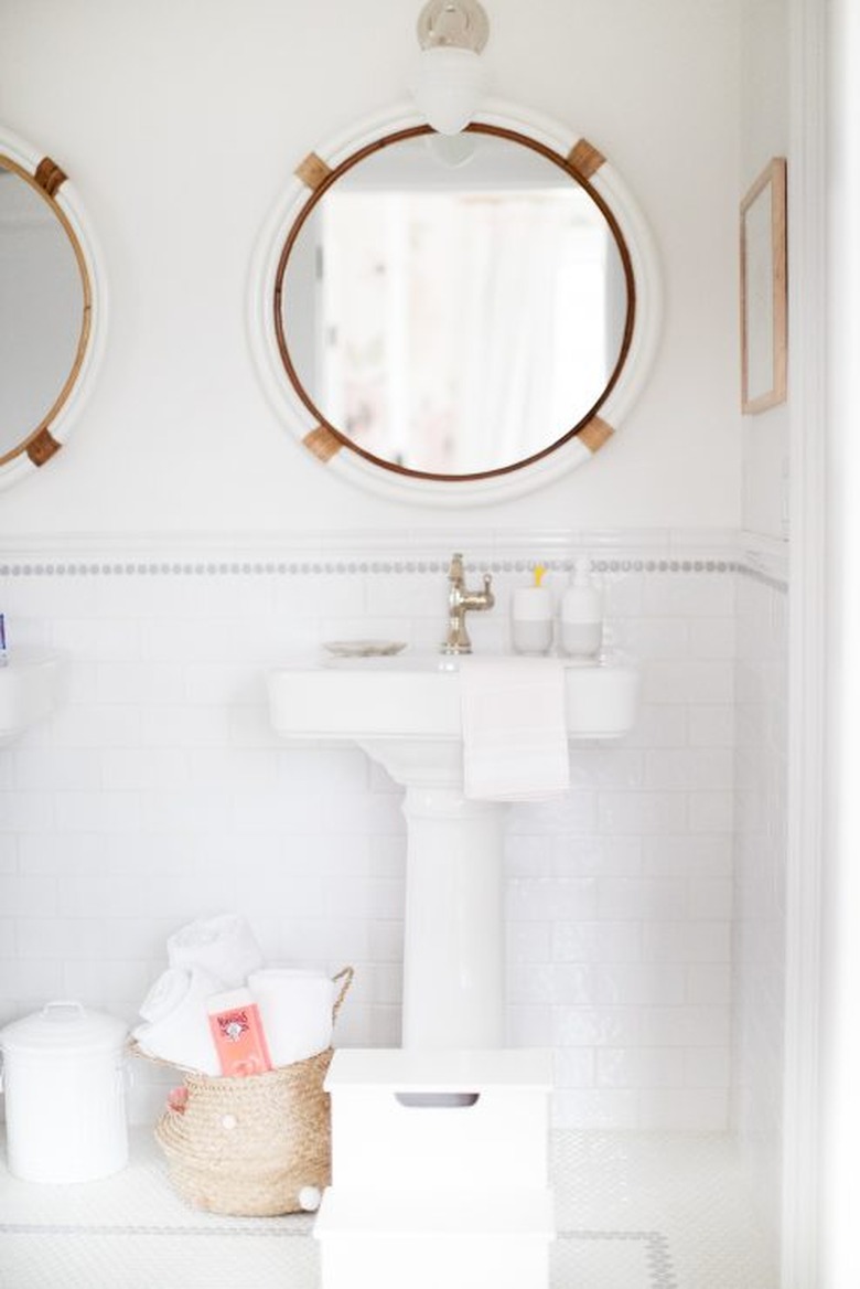 bathroom towel storage idea in white bathroom with round mirrors and pedestal sinks