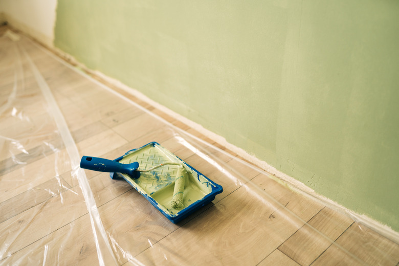 Newly opened can of white paint and paintbrush on wooden floor.