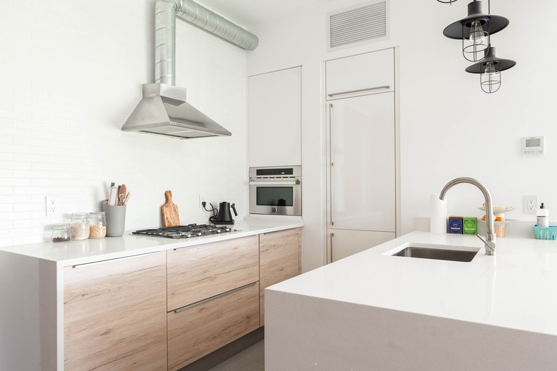 White contemporary kitchen with white countertops, wood cabinets, black stove burners, and silver sink and faucet