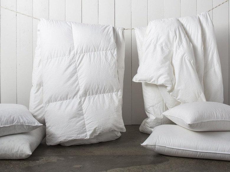 Two white duvets hanging from a clothesline in front of a white background.