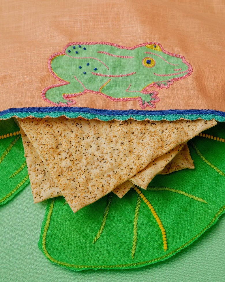 A light orange afikomen cover featuring an embroidered frog.