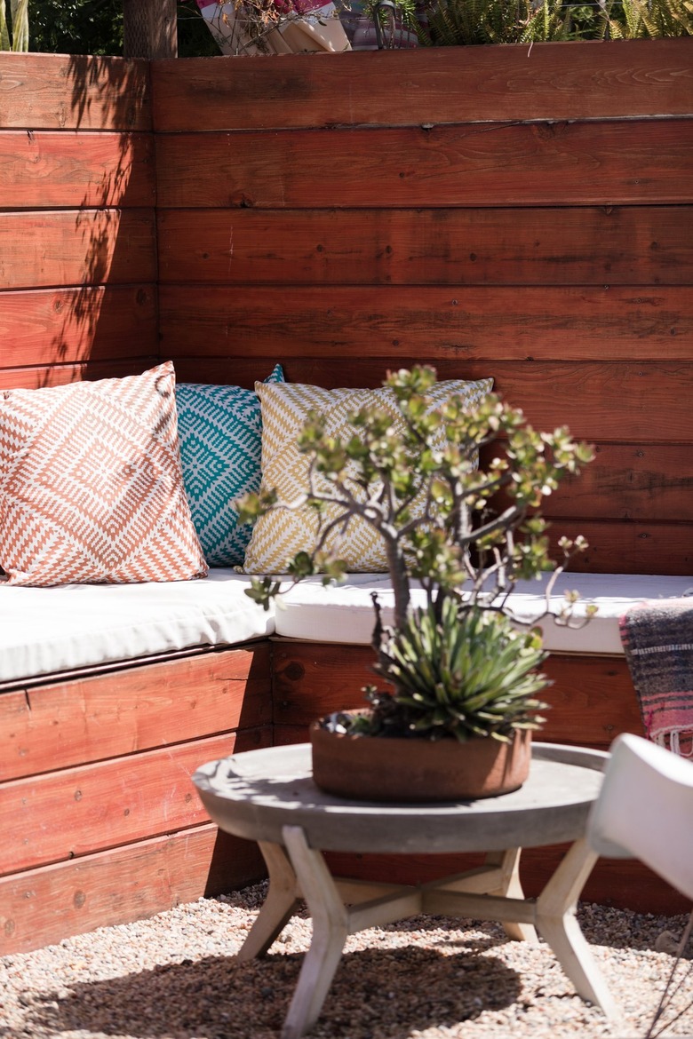 Outdoor wood bench, with white seat cushioning, and colorful accent pillows.