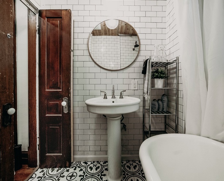 Pedestal Sink Storage Ideas in Bathroom with white pedestal sink, white subway tile, clawfoot tub, round mirror, metal shelves.