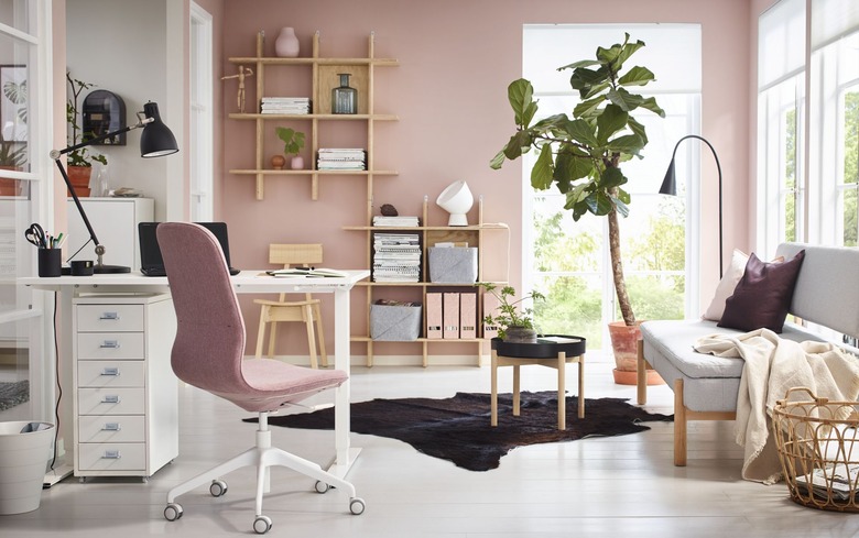 pink modern home office with plant and wall mounted shelves, sofa, and folding desk