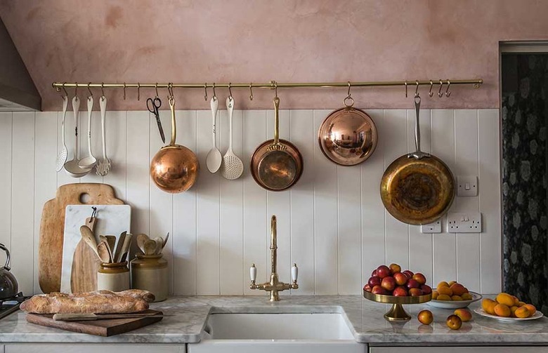 pink and white kitchen with copper pots hanging from a rack