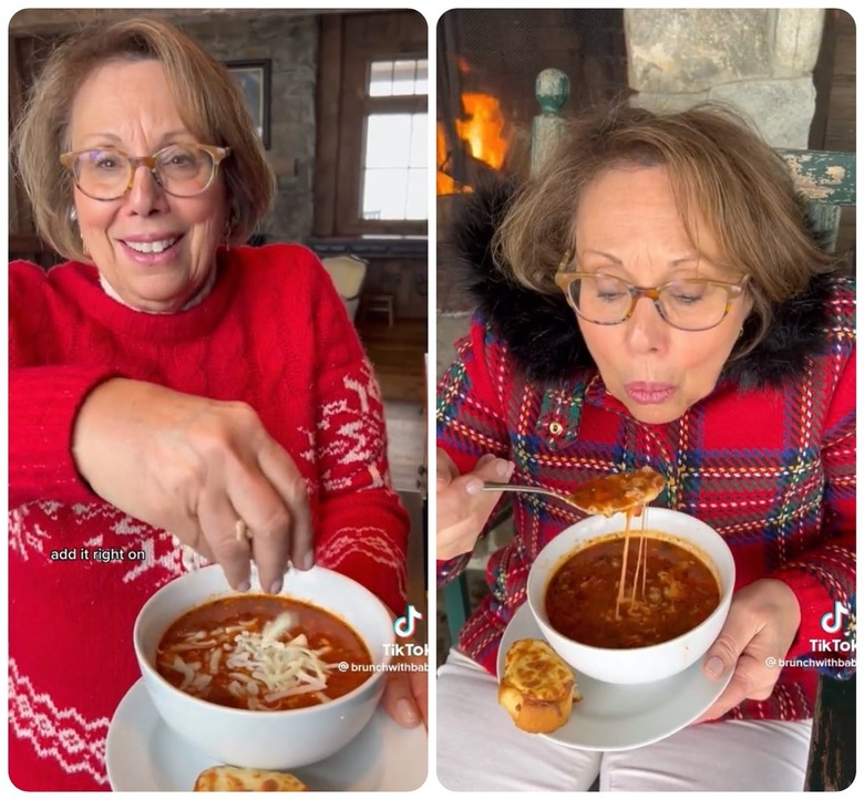 Two images, the image on the left shows TikTok creator @brunchwithbabs, an older white woman with short brown hair and glasses in a red sweater, sprinkling her pizza soup with mozzarella cheese. The second image is the TikTok creator sitting in a red plaid jacket with a black faux fur collar, blowing on a spoonful of soup, holding the bowl of soup with the other hand.