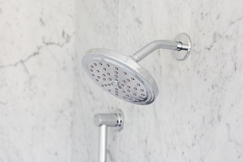 A silver rain shower head mounted on a gray granite or marble wall.