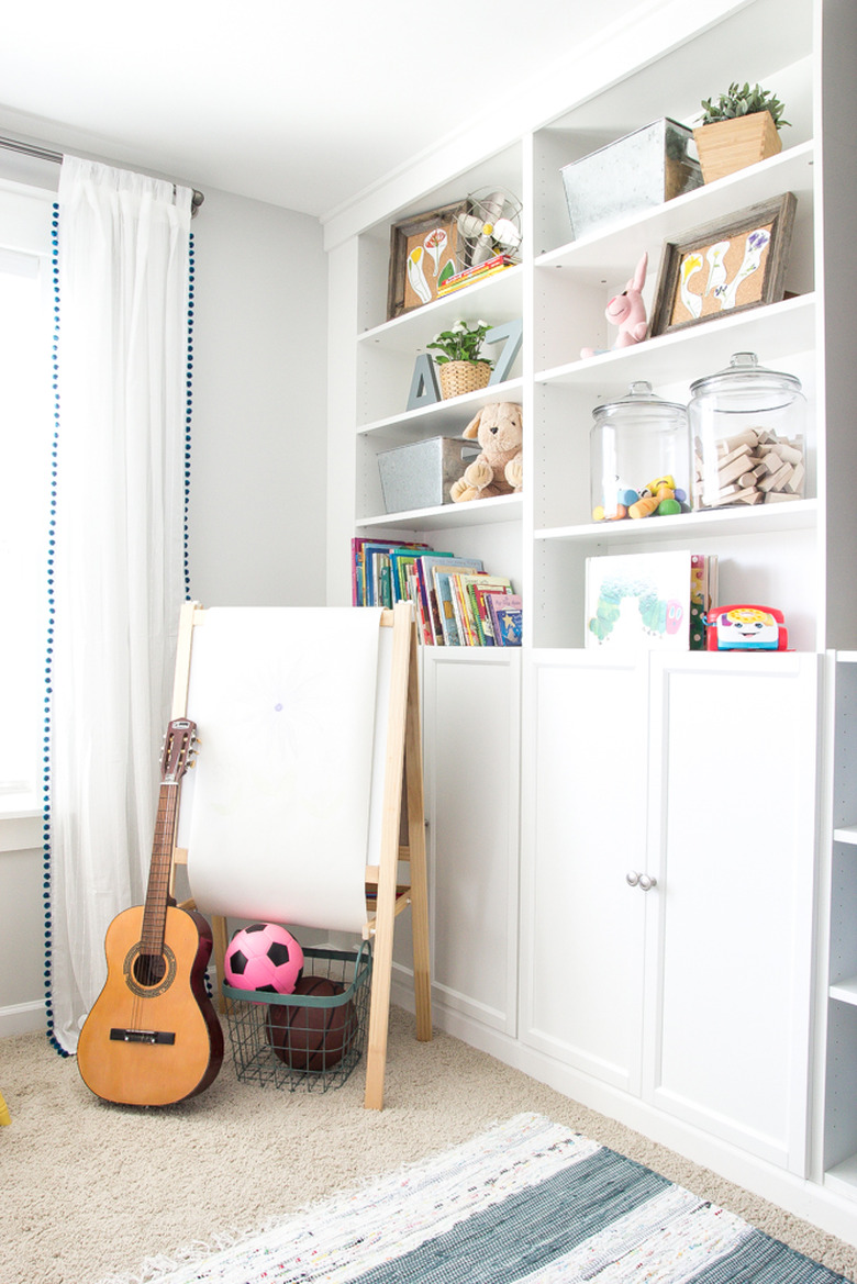 Built-in playroom storage idea with white shelving and drapery at window