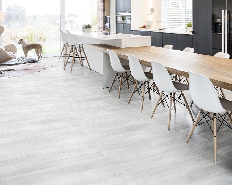 kitchen and dining space with wood table, black cabinets, and white chairs with light porcelain tile floor