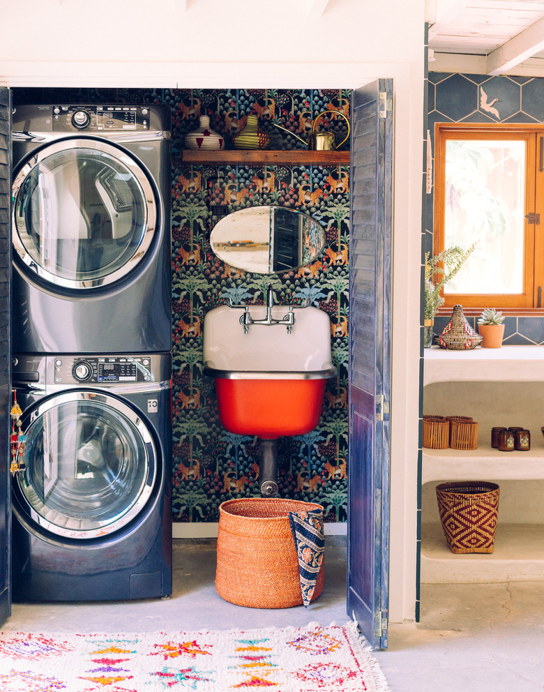 laundry room with wallpaper on wall and stacked washer and dryer next to sink