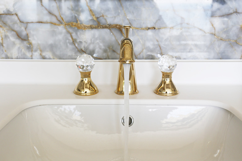 Closeup shot of white sink and gold or brass faucet.