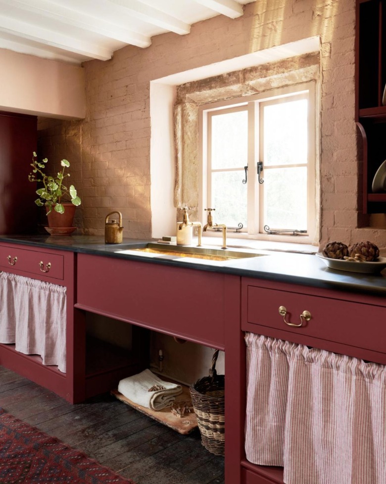 Kitchen with dark red cabinets, off-white brick walls, black counters.