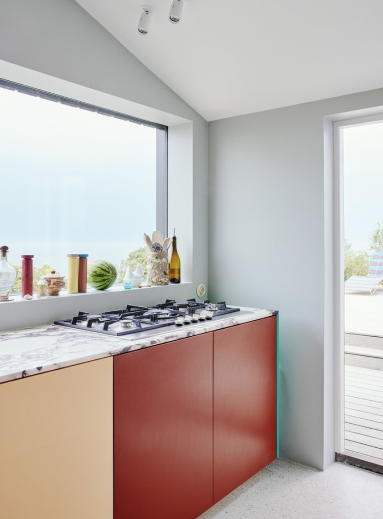 Modern kitchen with red and natural colored cabinets, marble counters, cooktop