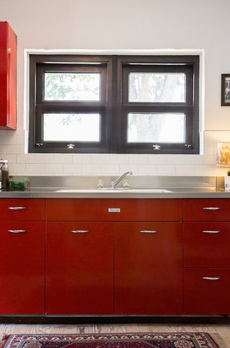 Red kitchen cabinets with a metal countertop and black window frames