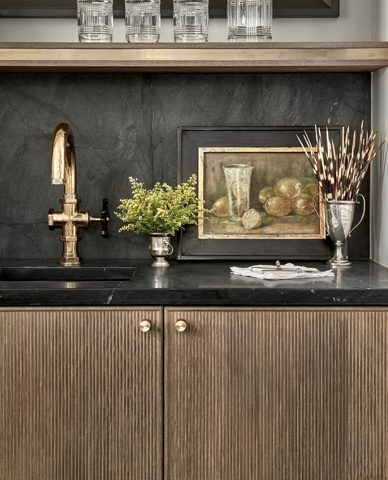 wood reeded cabinets with black countertop and backsplash