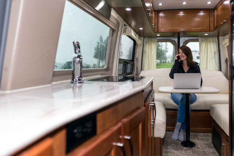 Young Woman Talking on phone and Using Laptop Inside Motorhome