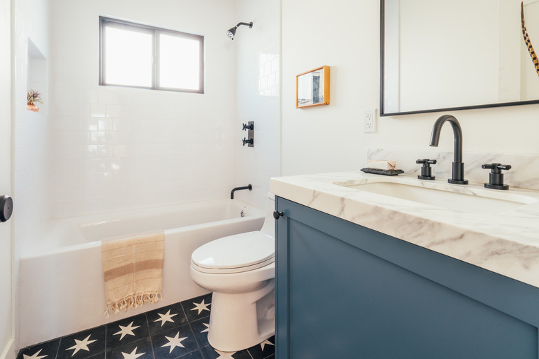 blue and stone bathroom vanity with sink, rectangular mirror with black trim, toilet, bathtub/shower combo and star-tiled floor