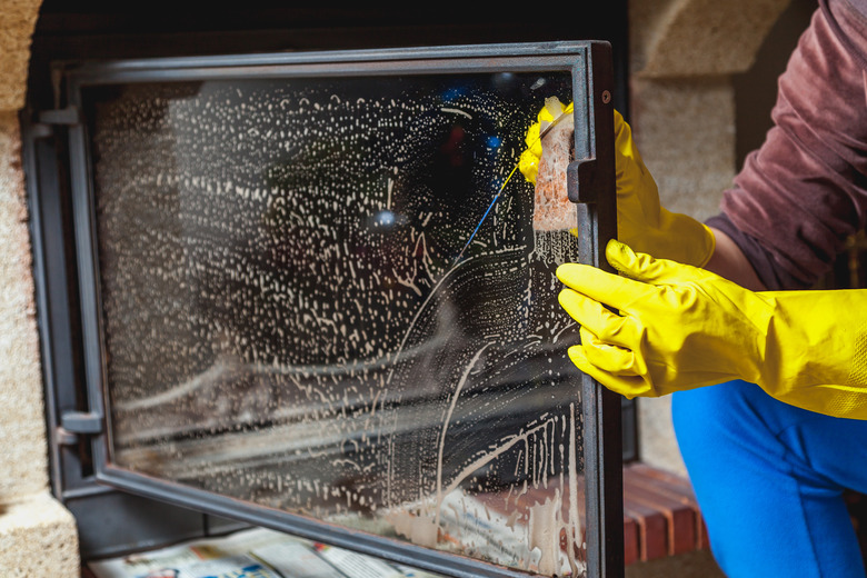 Hands in yellow gloves wash glass fireplace door