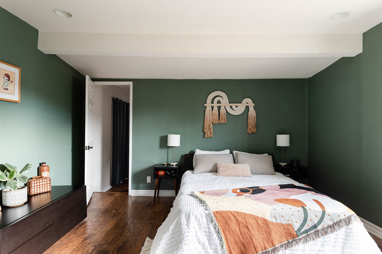 green bedroom with wood floors, white bed, artistic quilt