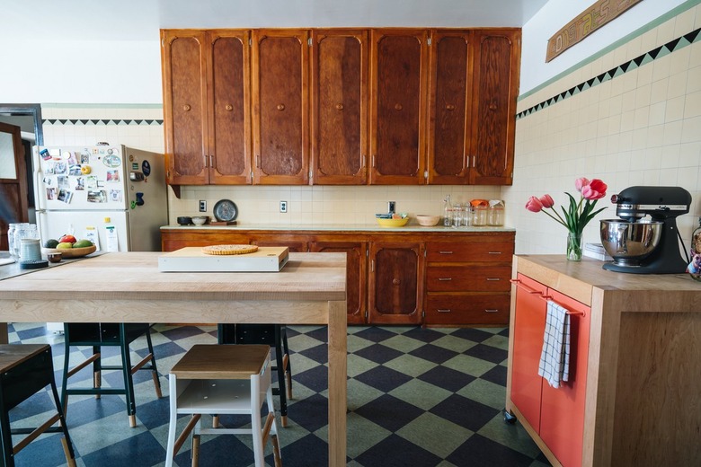 Kitchen with wood cabinets and dining table, stools, walls with beige tiles and triangle accent tiles, a portable cabinet with pink doors.