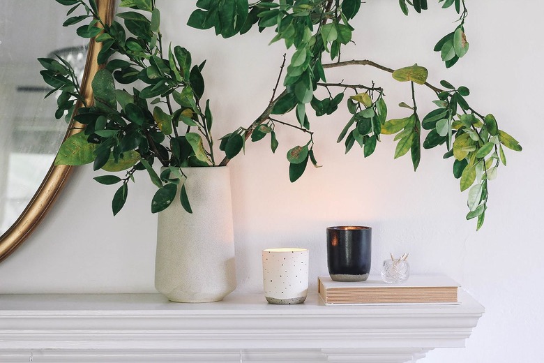 Mantel with lit black and white candle holders, book, crystal container of matches, and vase of leaves