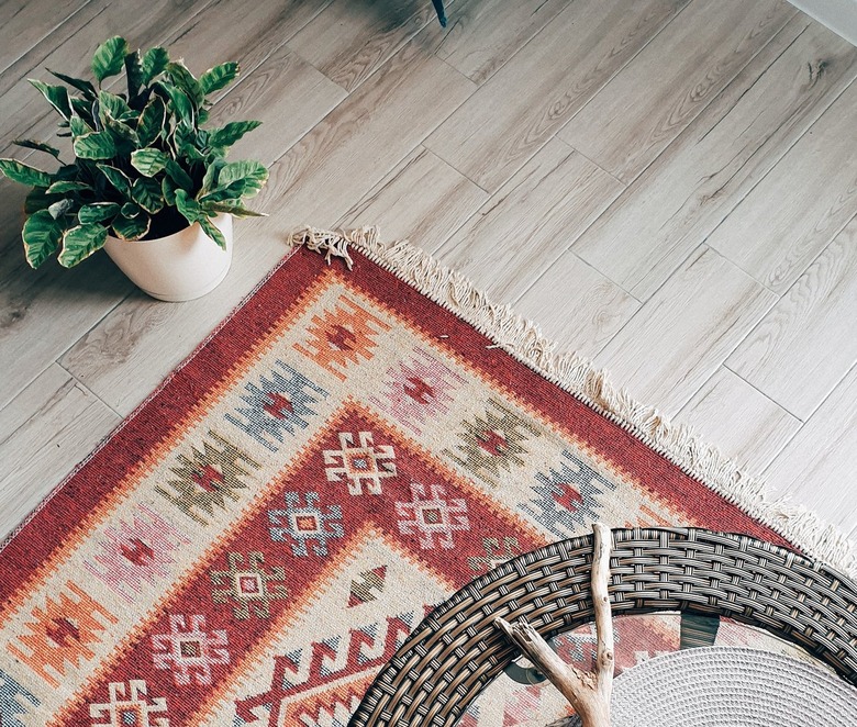 Corner of a patterned rug on a wooden floor next to a plant.