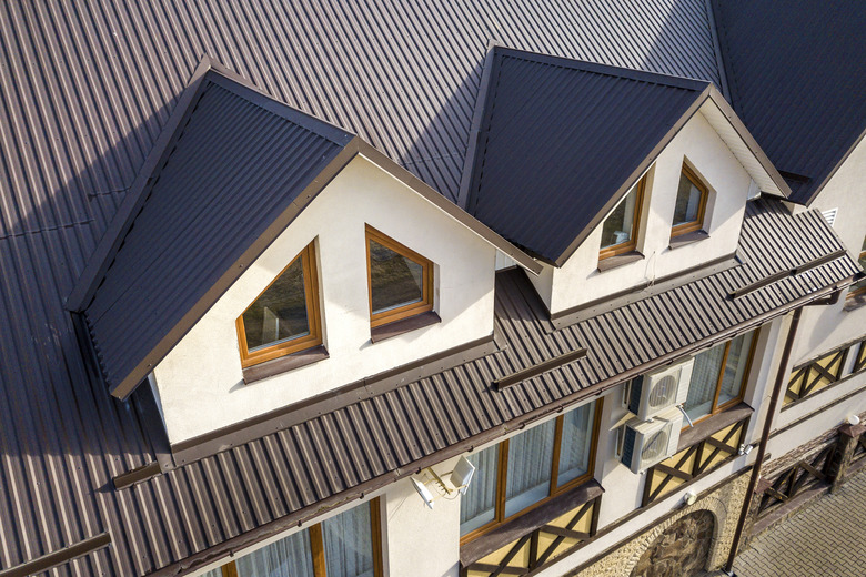 Close-up aerial view of building attic rooms exterior on metal shingle roof, stucco walls and plastic windows.