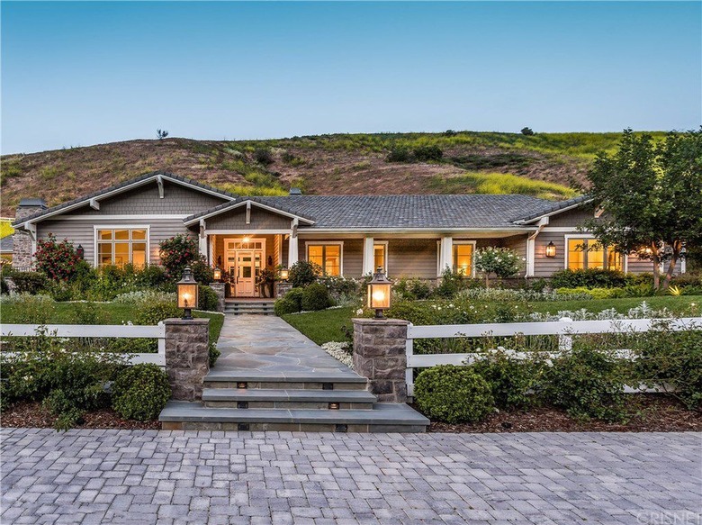 A ranch-style house with a concrete tile roof nestled against a green hill