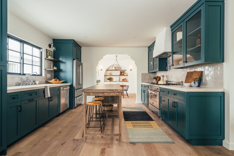 Kitchen with green painted cabinets, black hardware, a wood kitchen table island, and wood floor. Stainless steel appliances.