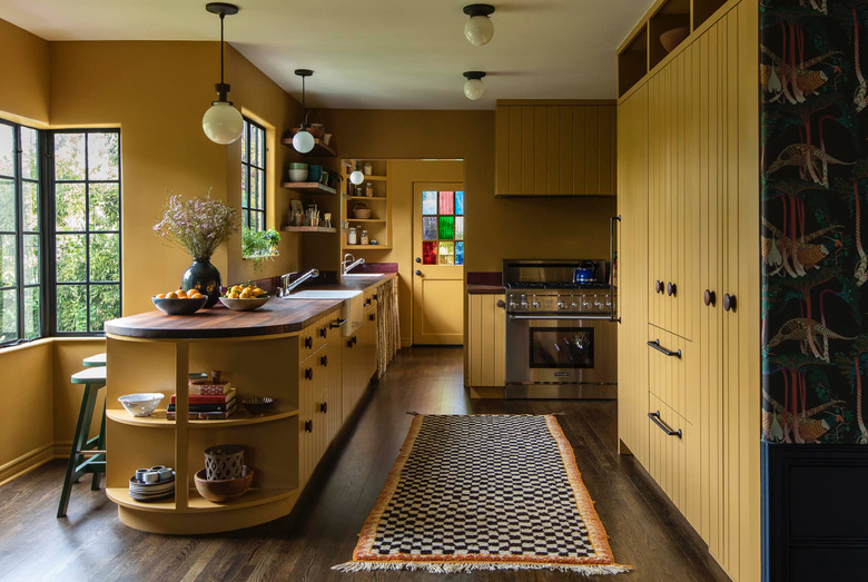 Kitchen with mustard yellow cabinets, dark wood floors, island with open curved shelves, wood counters, runner rug, stainless stove with rustic colors