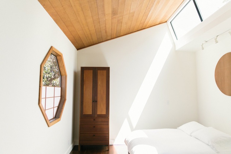 rustic decor in room with light wood paneled ceiling, arched ceiling, skylights, octagon window with panes and wood frame, white bedding, wood armoire.