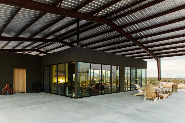 rustic industrial decor with corrugated metal and wood pergola over concrete patio with wood furniture.