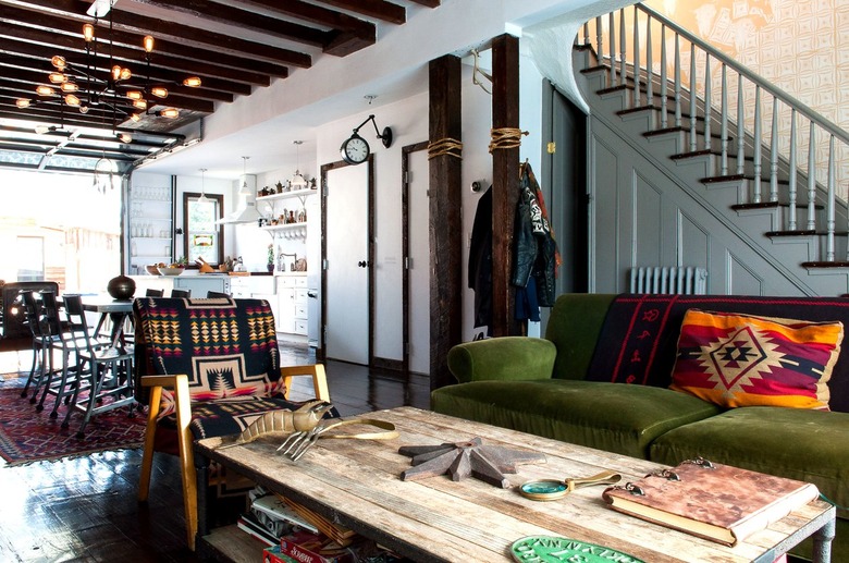 rustic industrial decor in a sitting room with a green couch, a rustic raw wood coffee table, and a staircase painted gray